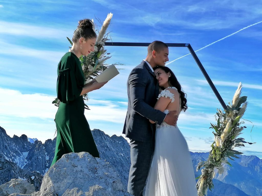 Elopement Brautpaar unter Blumenbogen auf einer Bergspitze mit Traurednerin Clara Diemling | Strauß & Fliege