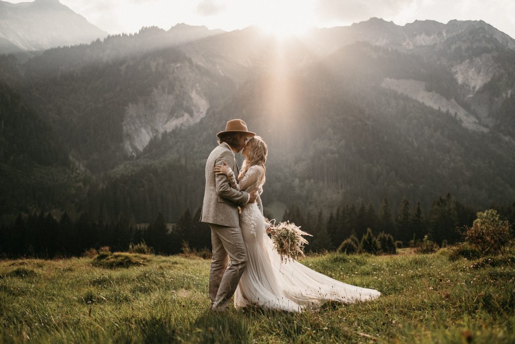 Strahlendes Brautpaar küsst sich beim Sonnenuntergang in den Alpen