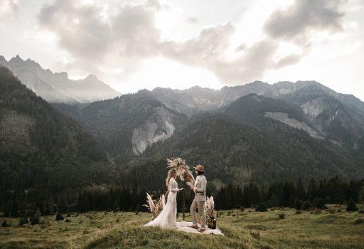 Elopement Brautpaar unter Blumenbogen auf einer Wiese mit Bergpanorama
