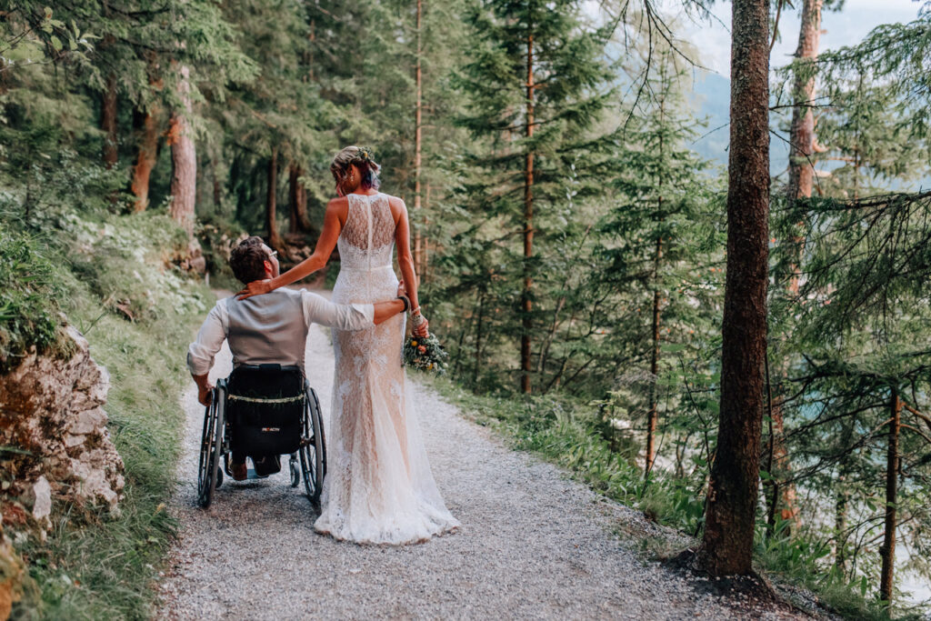 Bräutigam im Rollstuhl spaziert mit seiner Braut durch den Wald